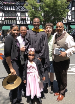 Lance Goodridge standing with his family and Lumbroso in front of Nassau street.  Lance is wearing his black masters graduation gown.