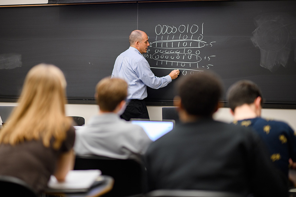 Alan Kaplan standing at the chalkboard in front of the class in COS 126.