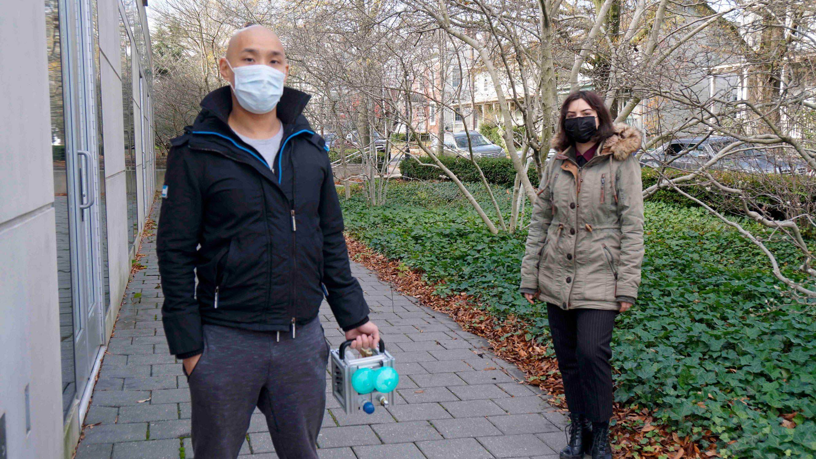 Daniel Suo and Paula Gradu standing outside of the Friend Center Building wearing masks.  Daniel is holding a medical device.