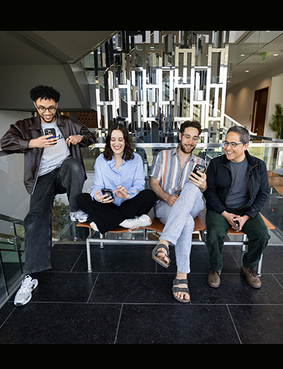 Four researchers sitting together on a bench, smiling and looking at their phones