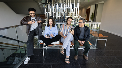 Four researchers sitting together on a bench, smiling and looking at their phones