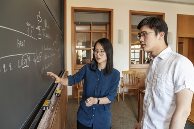 Danqi Chen standing at a blackboard with Zexuan Zhong, CS graduate student.