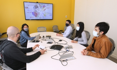 Yuri Pritykin and his lab group sitting around table in a conference room.  They discuss a slide with a cluster graph on the TV monitor on the wall.