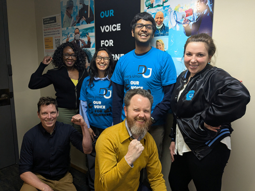 Six people standing in front of a poster smiling