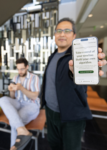 A professor holds out his phone, where the text reads: "Take control of your timeline. Build your own algorithm"