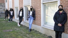 Photo of five students standing along a wall outside of a building at E-Quad.