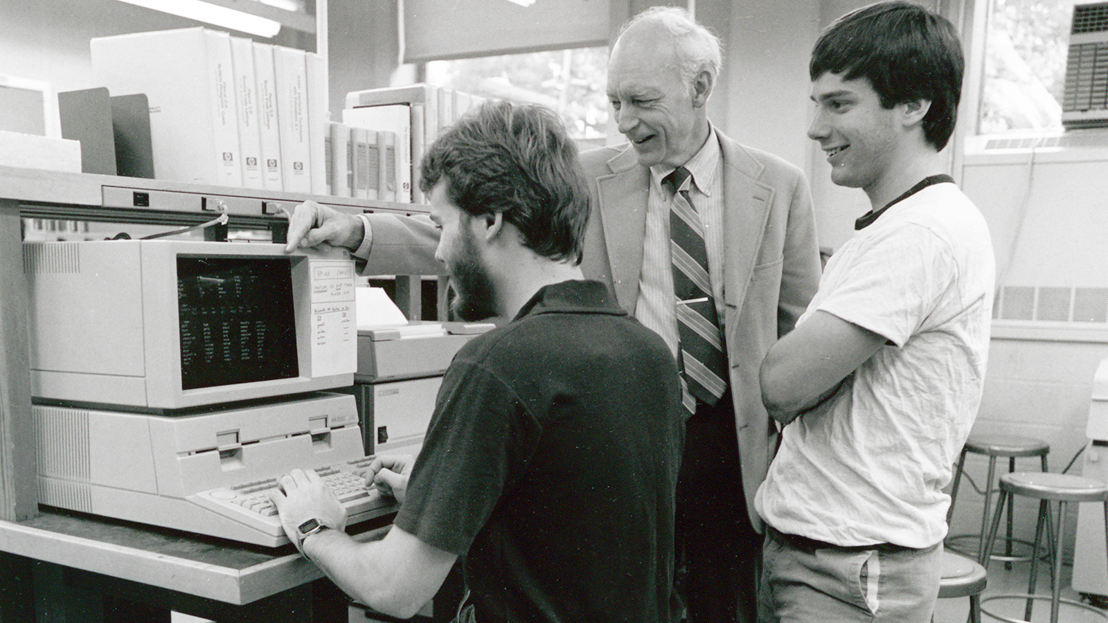 Photo from 1985 of Bruce Arden with two students working on an early personal computer.