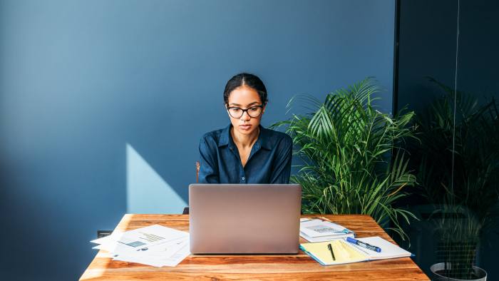 A woman behind a table, looking at her laptop screen 